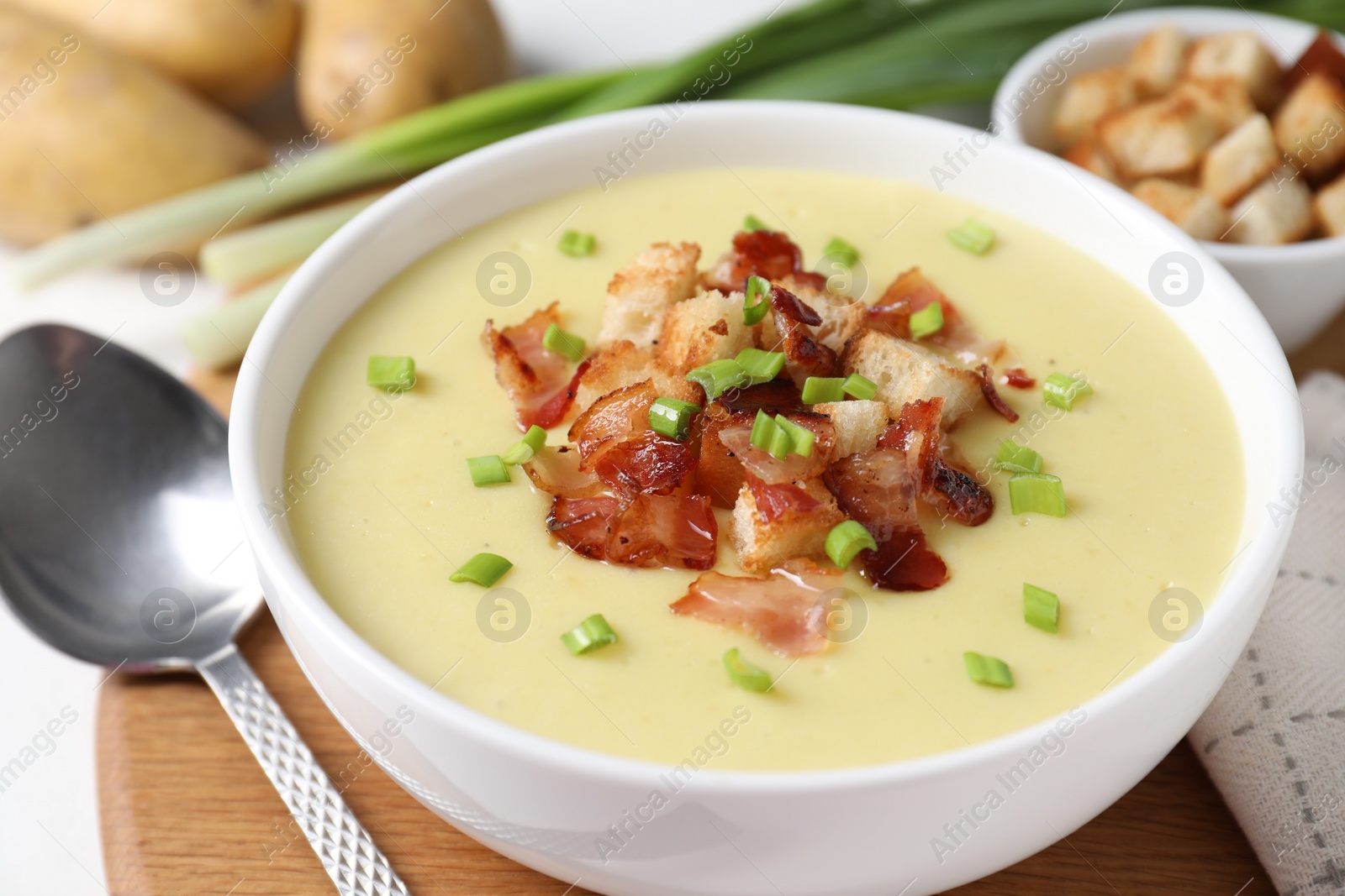 Photo of Tasty potato soup with bacon in bowl and spoon on white table, closeup