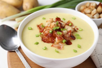 Tasty potato soup with bacon in bowl and spoon on white table, closeup