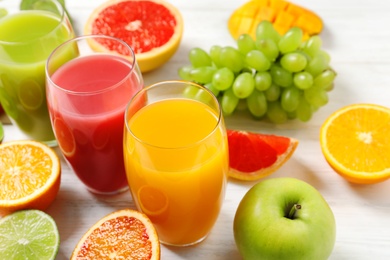 Photo of Glasses with different juices and fresh fruits on wooden table