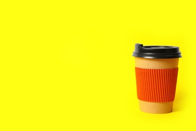 Photo of Takeaway paper coffee cup with cardboard sleeve on yellow background. Space for text