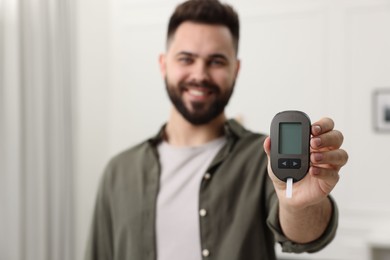 Diabetes test. Happy man showing glucometer at home, selective focus