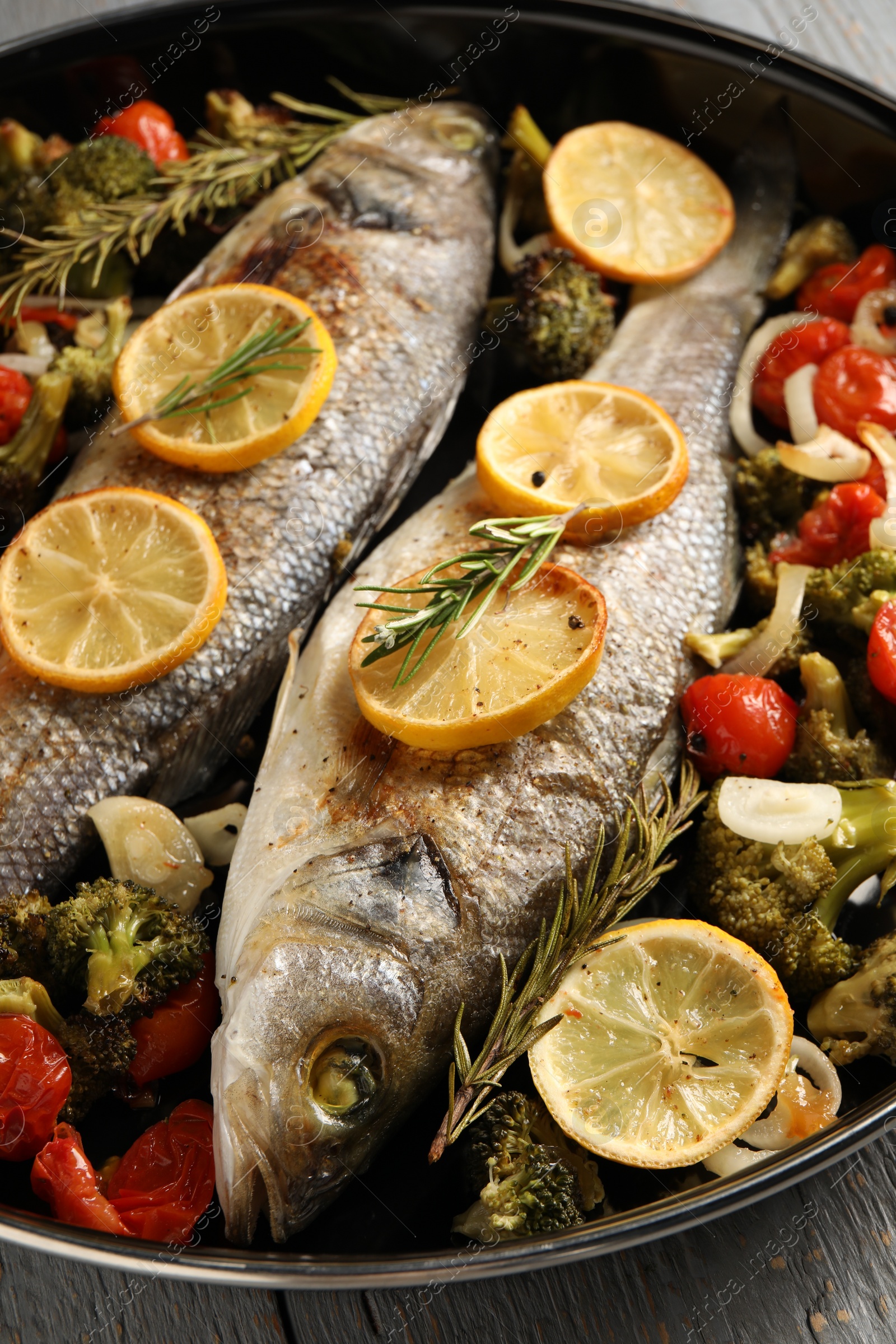 Photo of Baked fish with vegetables, rosemary and lemon on grey wooden table, closeup