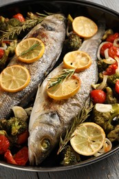 Baked fish with vegetables, rosemary and lemon on grey wooden table, closeup