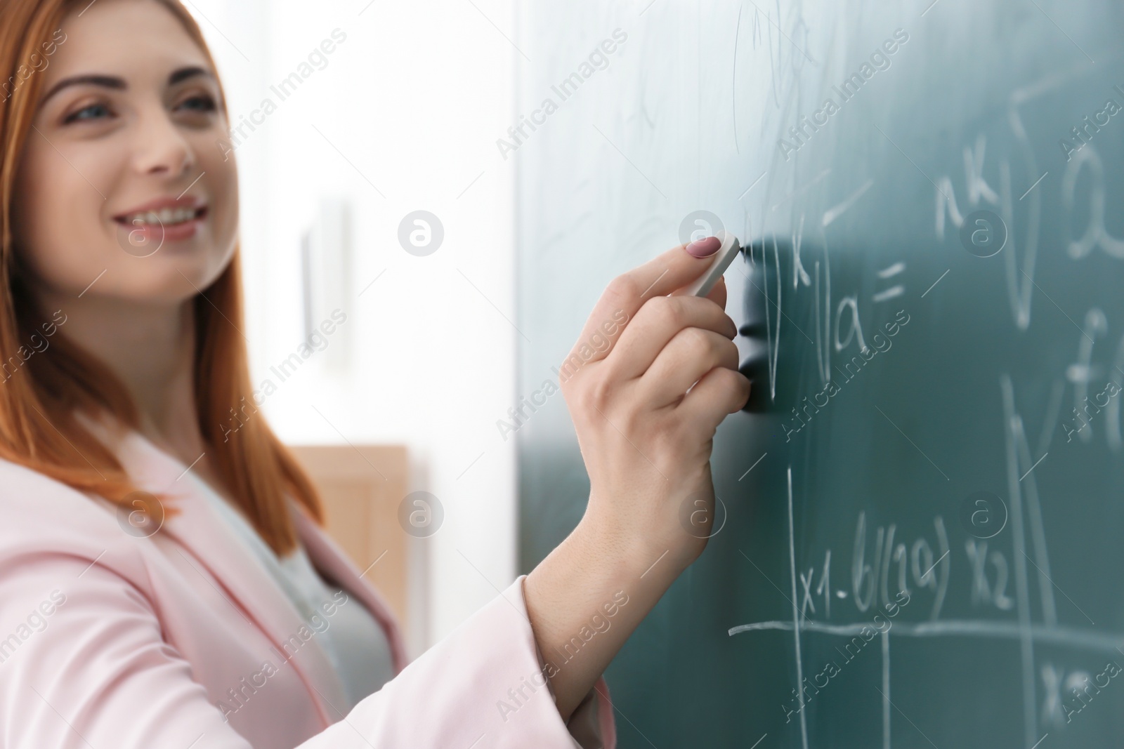 Photo of Beautiful young teacher writing on blackboard in classroom