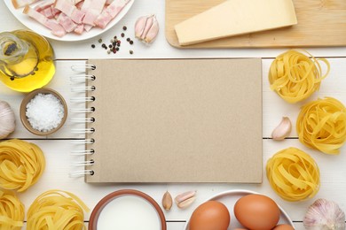 Blank recipe book surrounded by different ingredients on white wooden table, flat lay. Space for text