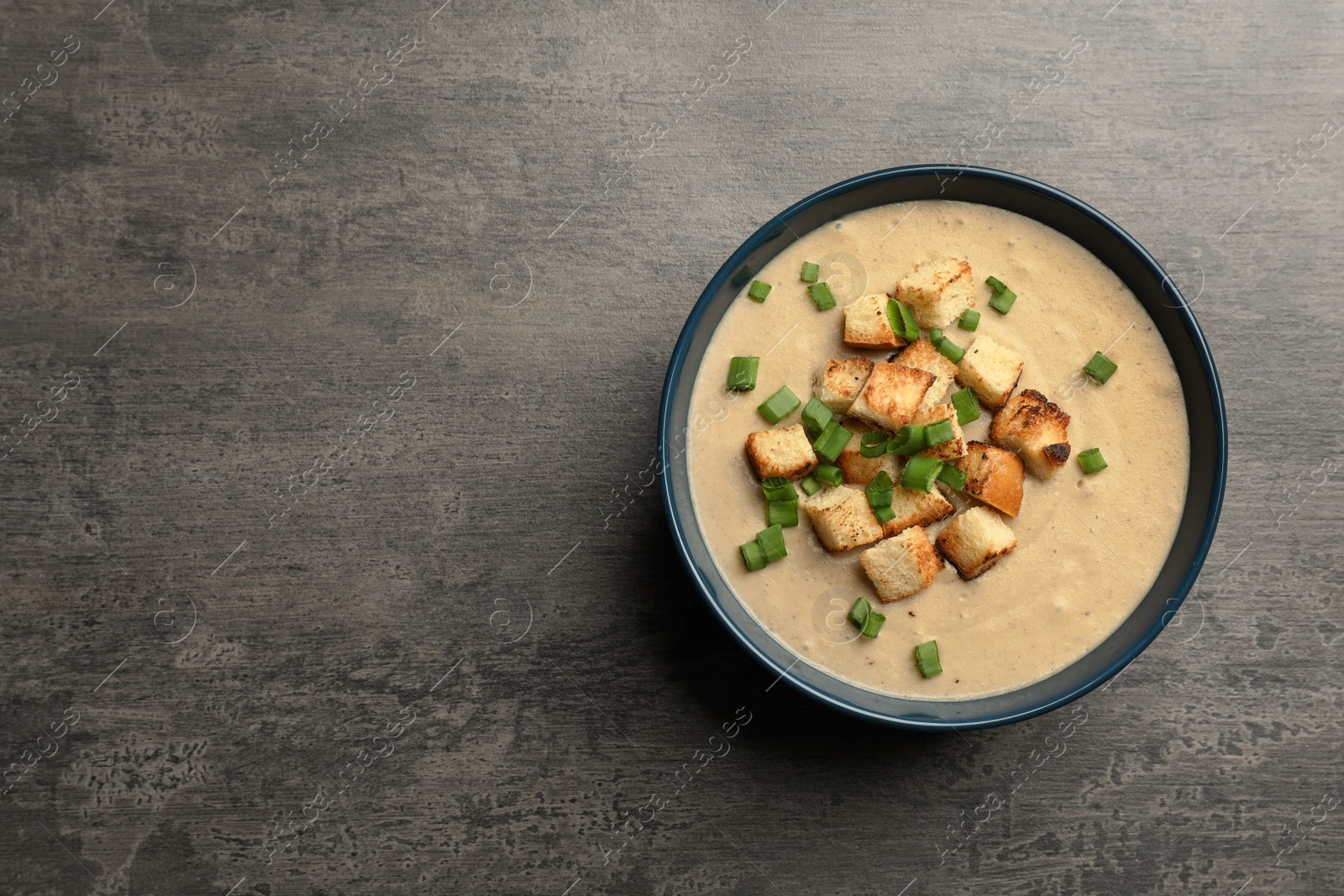 Photo of Bowl of fresh homemade mushroom soup on gray background, top view with space for text