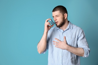 Young man using asthma inhaler on color background with space for text