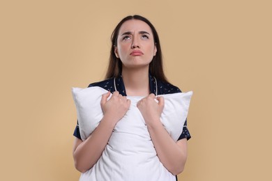 Tired young woman with pillow on beige background. Insomnia problem