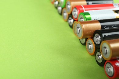 New AA batteries on light green background, closeup. Space for text