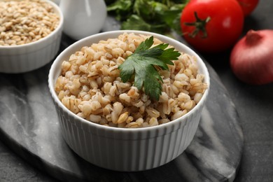 Photo of Tasty pearl barley porridge and parsley in bowl on dark textured table, closeup