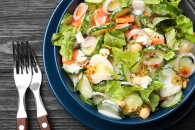 Bowl of delicious cucumber salad served on black wooden table, flat lay