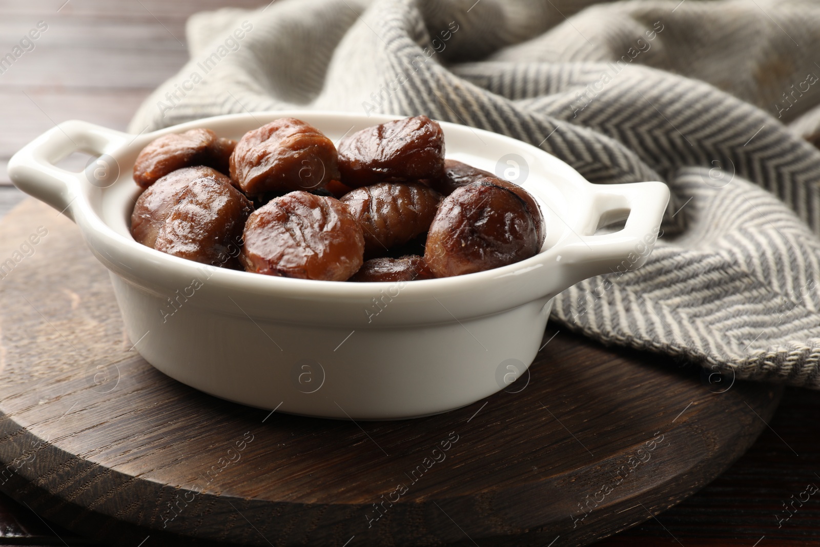 Photo of Roasted edible sweet chestnuts in dish on light wooden table