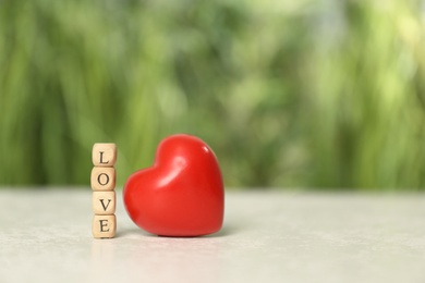 Photo of Word Love made of small wooden cubes with letters near red decorative heart on light table