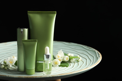 Photo of Set of cosmetic products and flowers on table against black background. Space for text