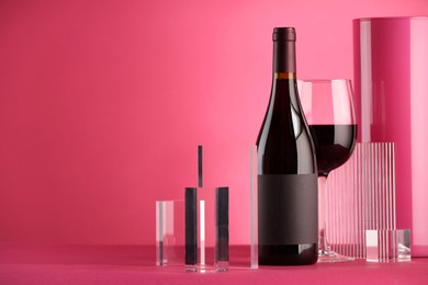 Stylish presentation of delicious red wine in bottle and glass on pink background. Space for text