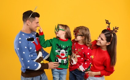 Family in Christmas sweaters and festive accessories on yellow background