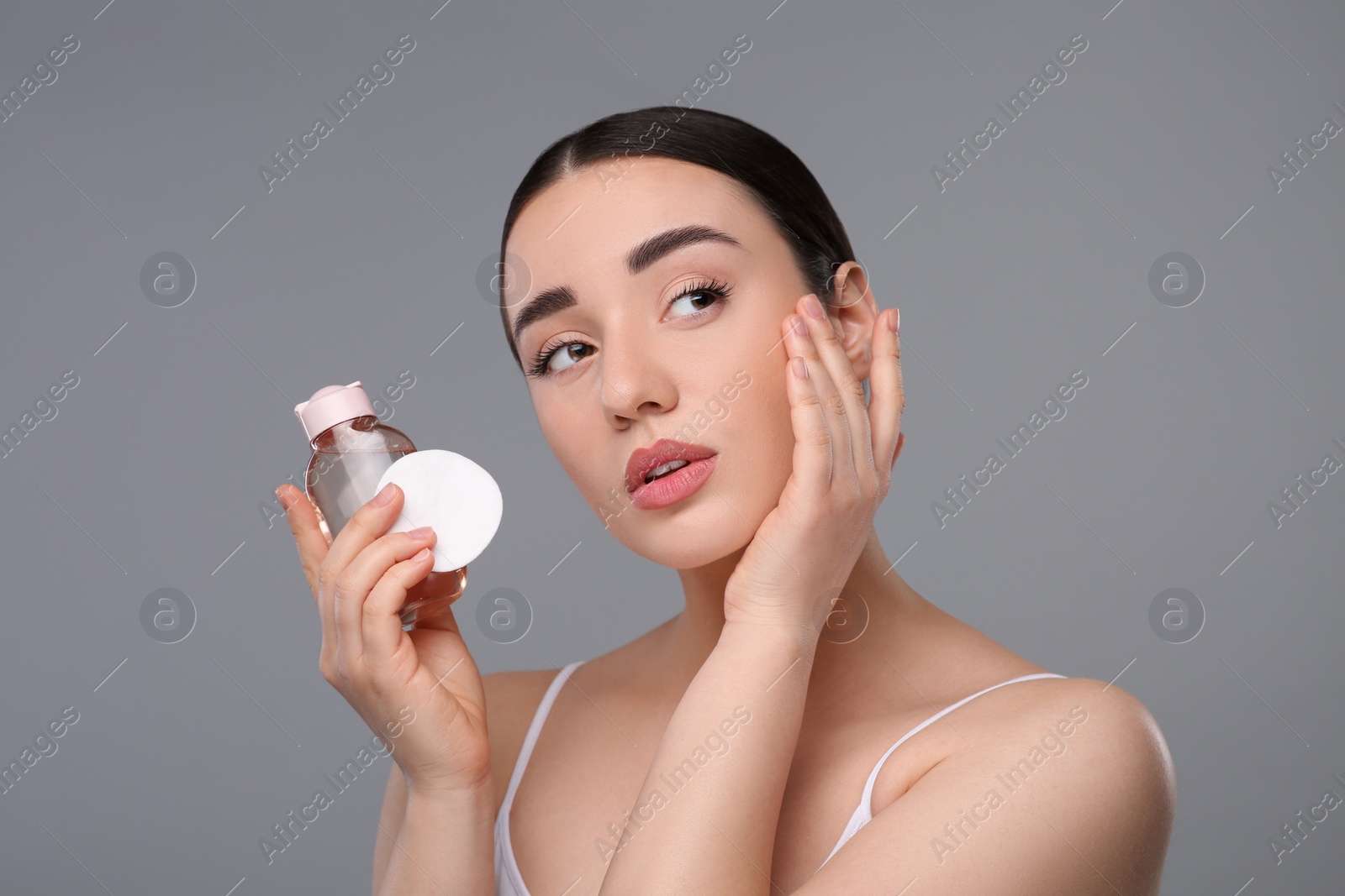 Photo of Beautiful woman with makeup remover and cotton pad on gray background