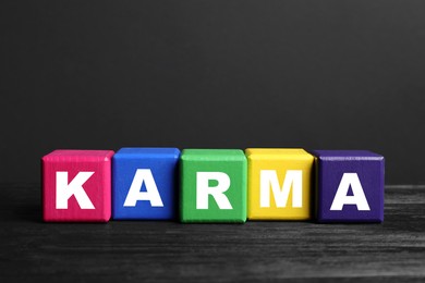 Photo of Word Karma made of colorful cubes with letters on black wooden table