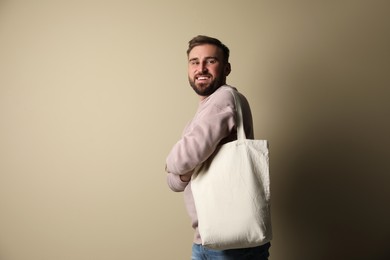 Happy young man with eco bag on beige background. Space for text