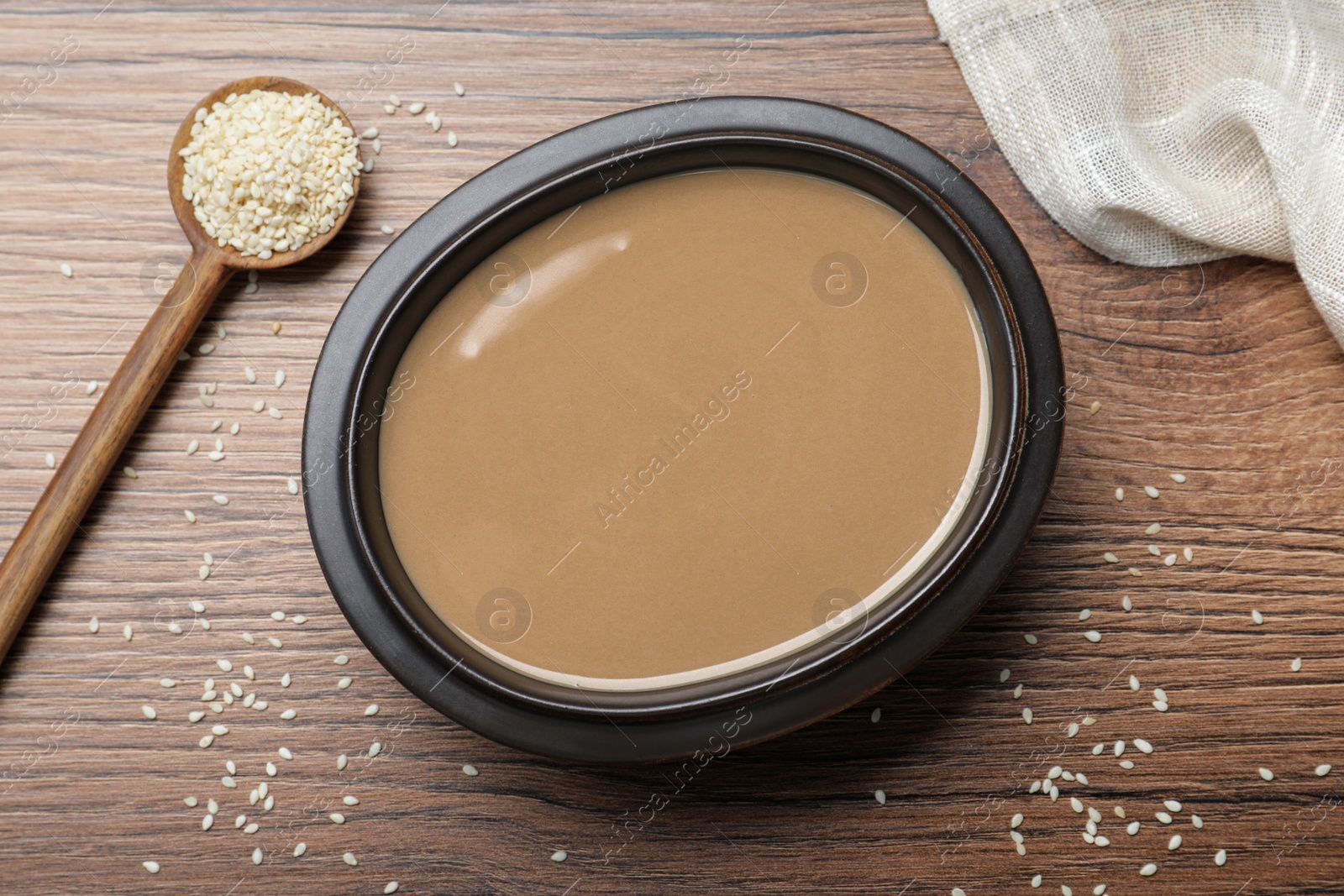 Photo of Tasty sesame paste, seeds and spoon on wooden table, flat lay