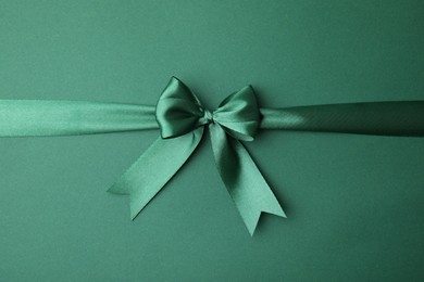Photo of Bright satin ribbon with bow on green background, top view