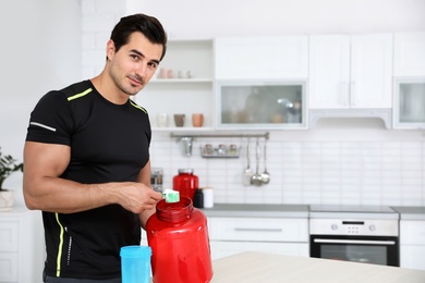 Young athletic man preparing protein shake in kitchen, space for text