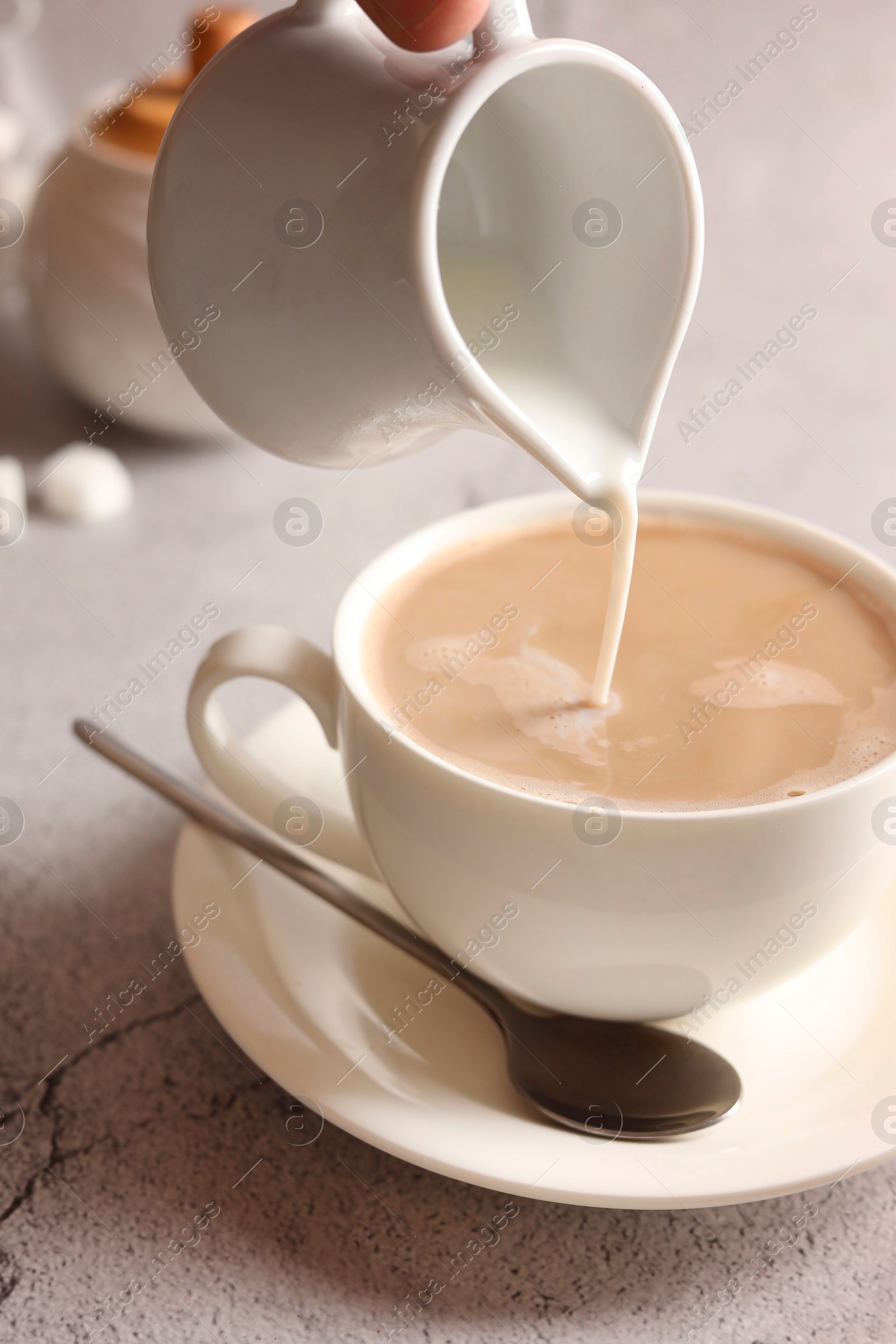 Photo of Pouring milk into cup with coffee on light grey textured table, closeup