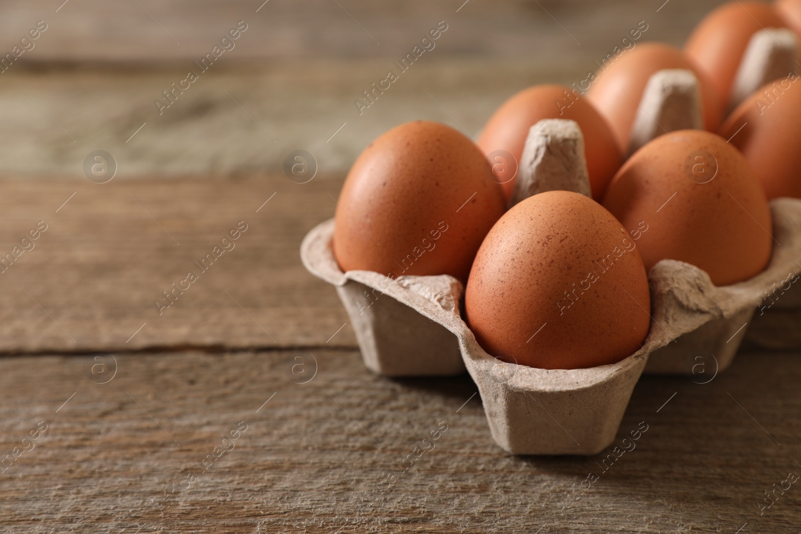 Photo of Raw chicken eggs in carton on wooden table, closeup. Space for text