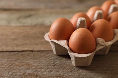 Raw chicken eggs in carton on wooden table, closeup. Space for text