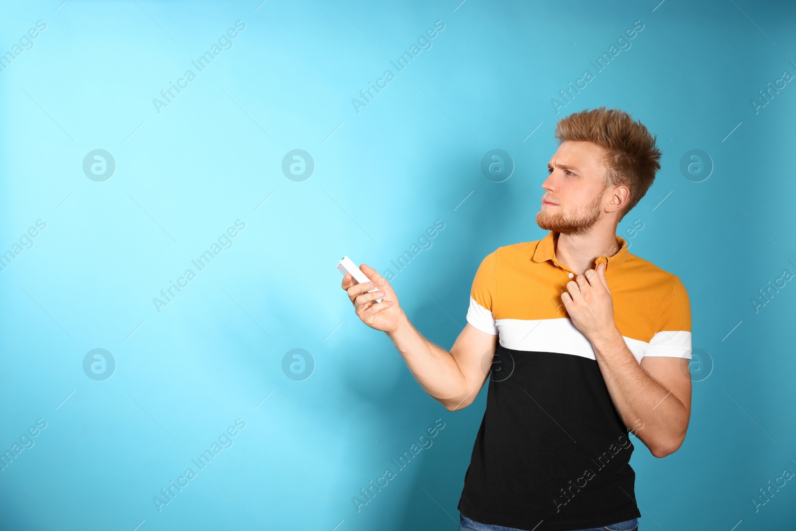 Photo of Young man with air conditioner remote on blue background. Space for text