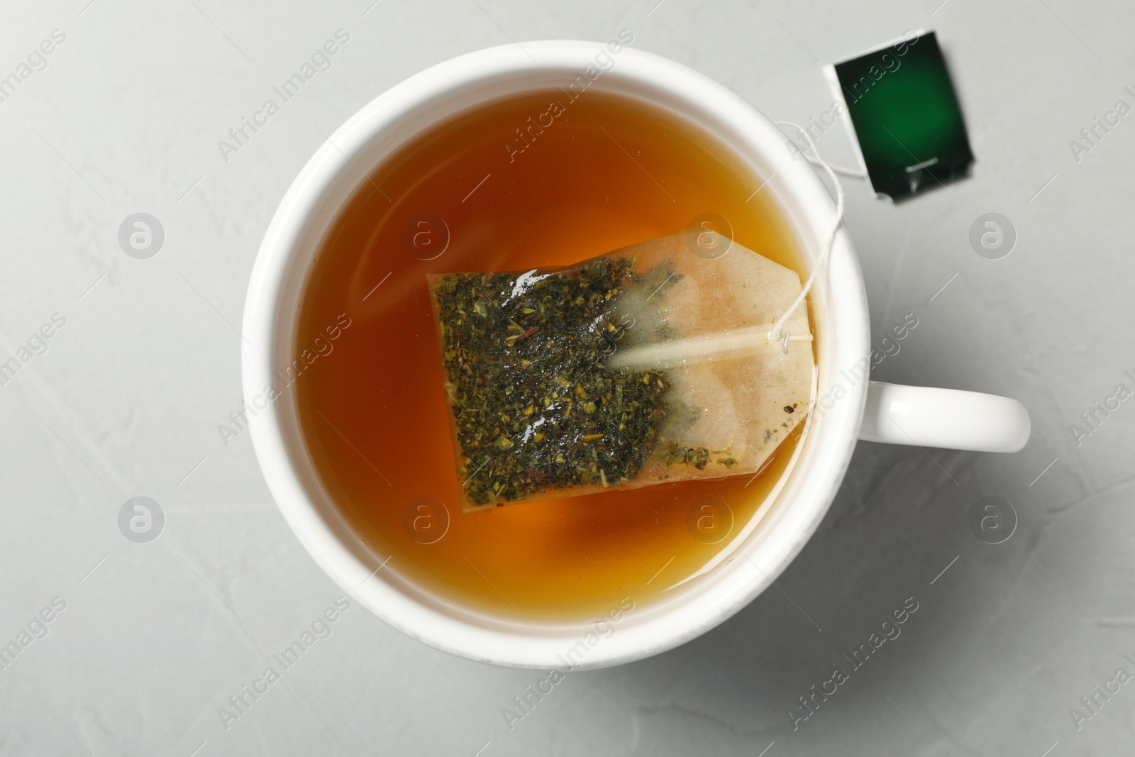 Photo of Tea bag in cup of hot water on light grey table, top view