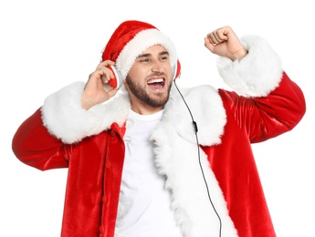 Young man in Santa costume listening to Christmas music on white background