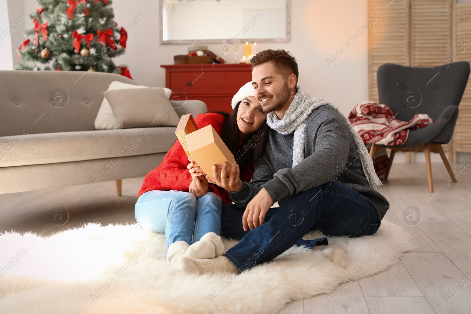 Photo of Young man giving gift box to girlfriend at home. Happy couple celebrating Christmas