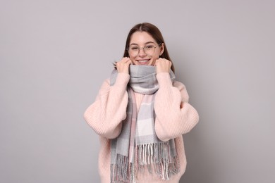 Beautiful woman in warm scarf and glasses on gray background