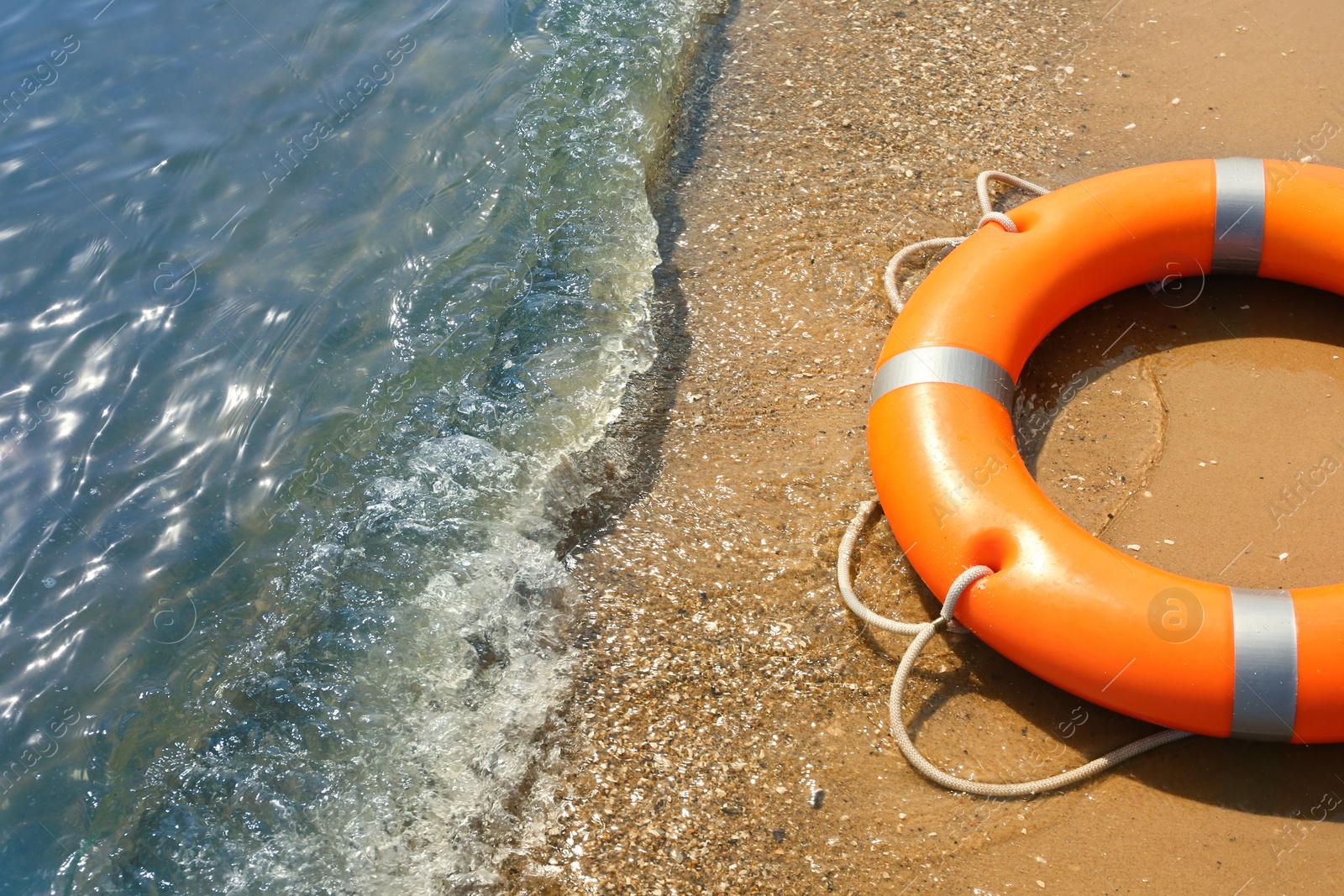 Photo of Orange life buoy on sand near sea, closeup. Emergency rescue equipment