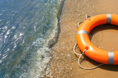 Photo of Orange life buoy on sand near sea, closeup. Emergency rescue equipment