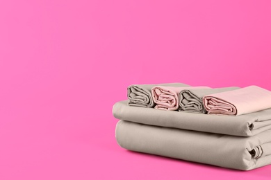 Photo of Stack of clean bed sheets on pink background. Space for text