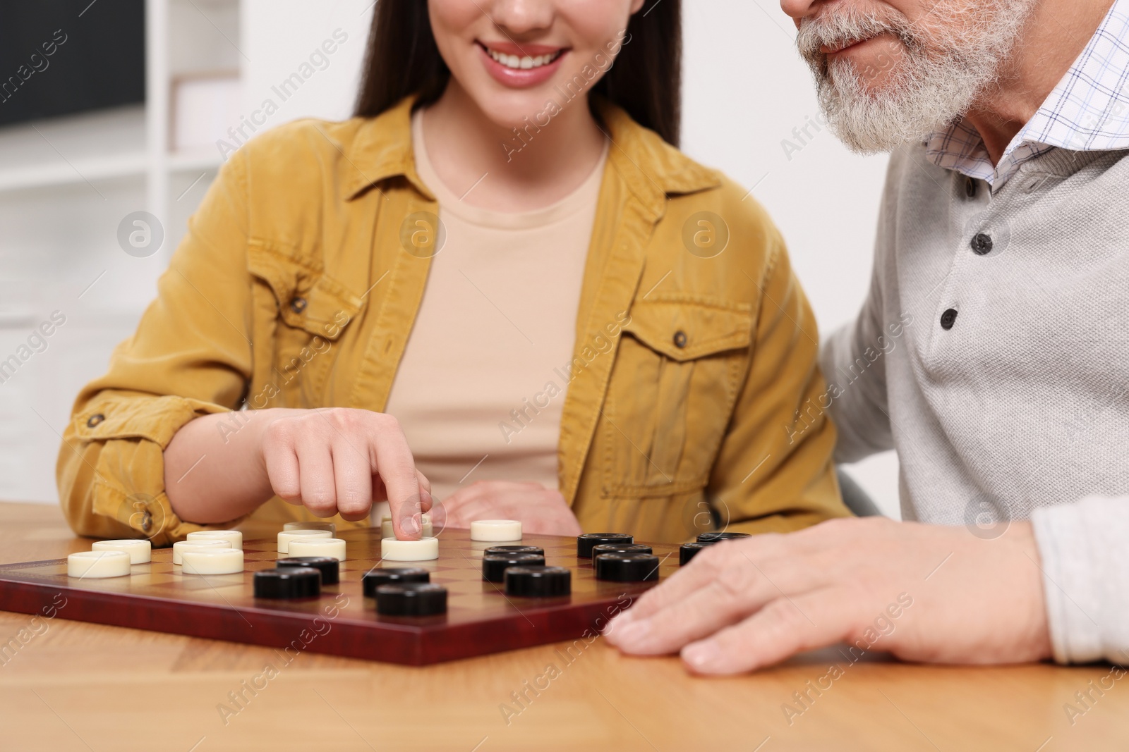 Photo of Playing checkers. Senior man learning woman at table in room, closeup