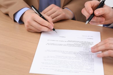 Photo of Businesspeople signing contract at wooden table, closeup of hands