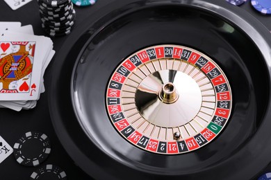Photo of Roulette wheel, playing cards and chips on table, closeup. Casino game