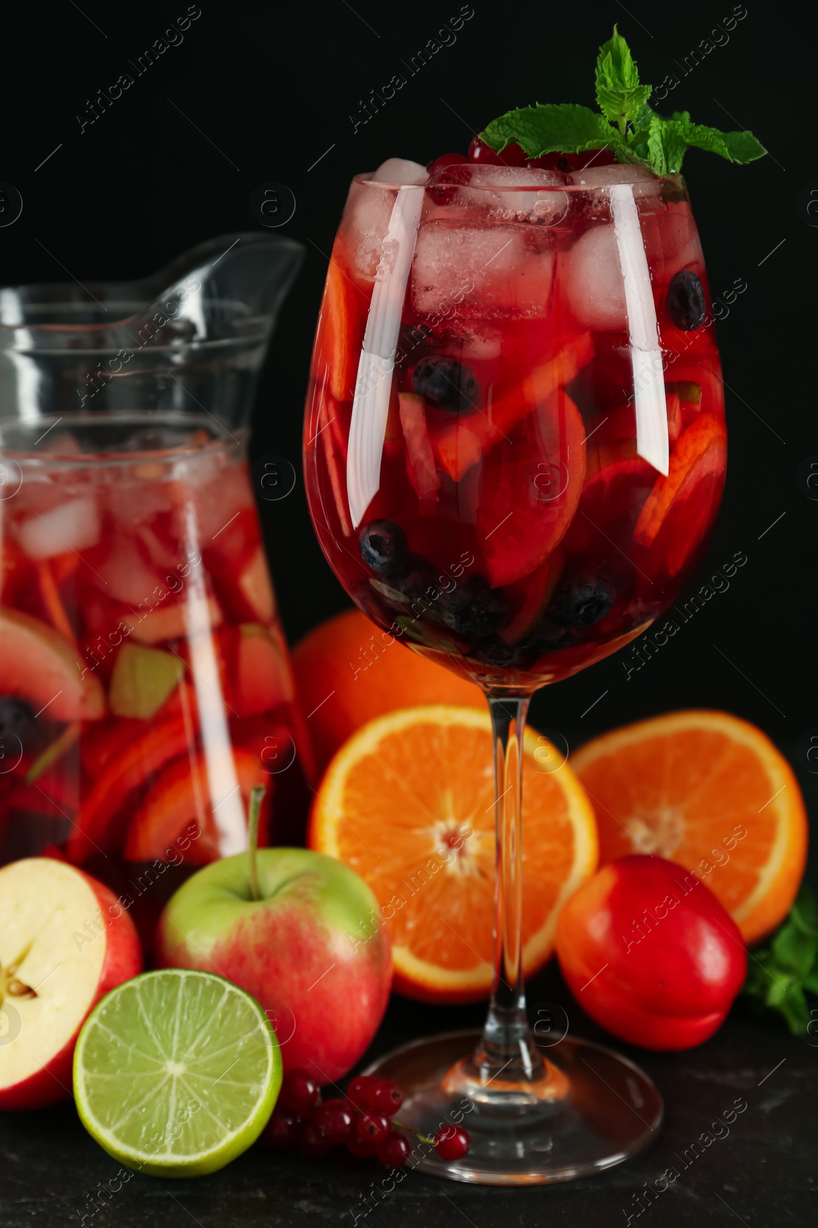 Photo of Glass and jug of Red Sangria with fruits on black table