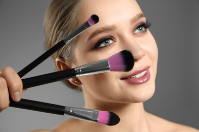 Beautiful woman with makeup brushes on light grey background