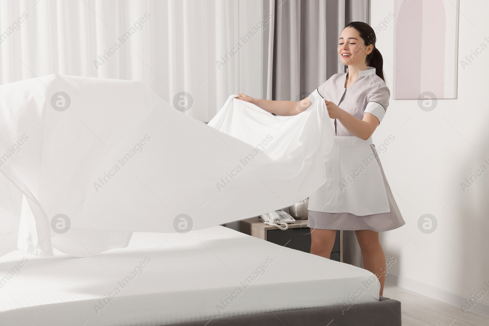 Photo of Young maid making bed in hotel room