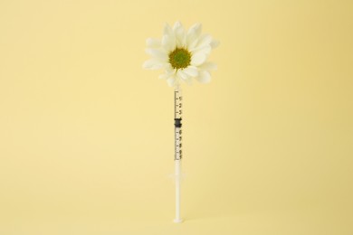 Medical syringe and chrysanthemum flower on pale yellow background