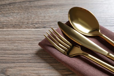 Photo of Set of golden cutlery with napkin on wooden table, closeup. Space for text