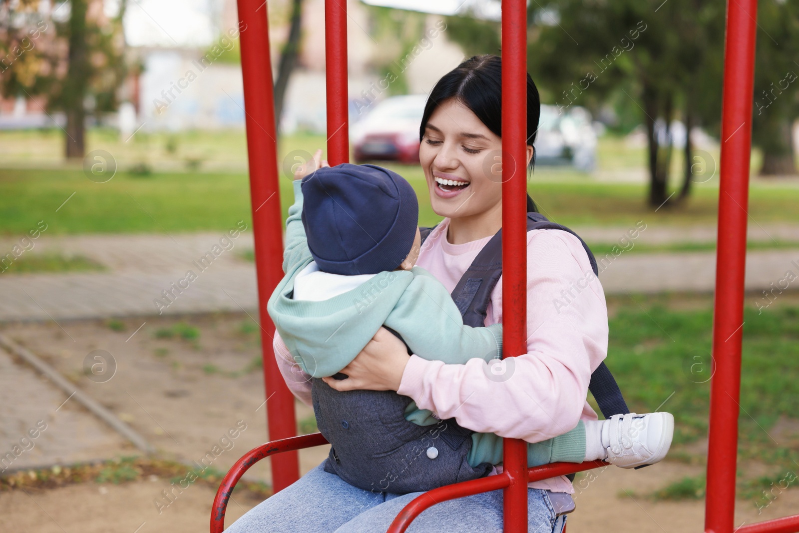 Photo of Mother holding her child in sling (baby carrier) on swing outdoors