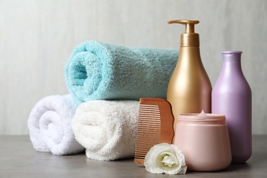 Photo of Different hair products, rolled towels and wooden comb on grey table