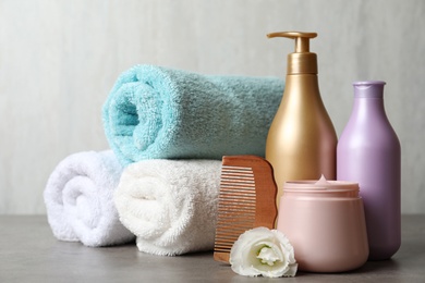 Different hair products, rolled towels and wooden comb on grey table