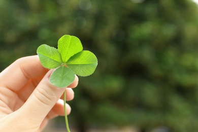 Photo of Woman holding four-leaf clover outdoors, closeup with space for text