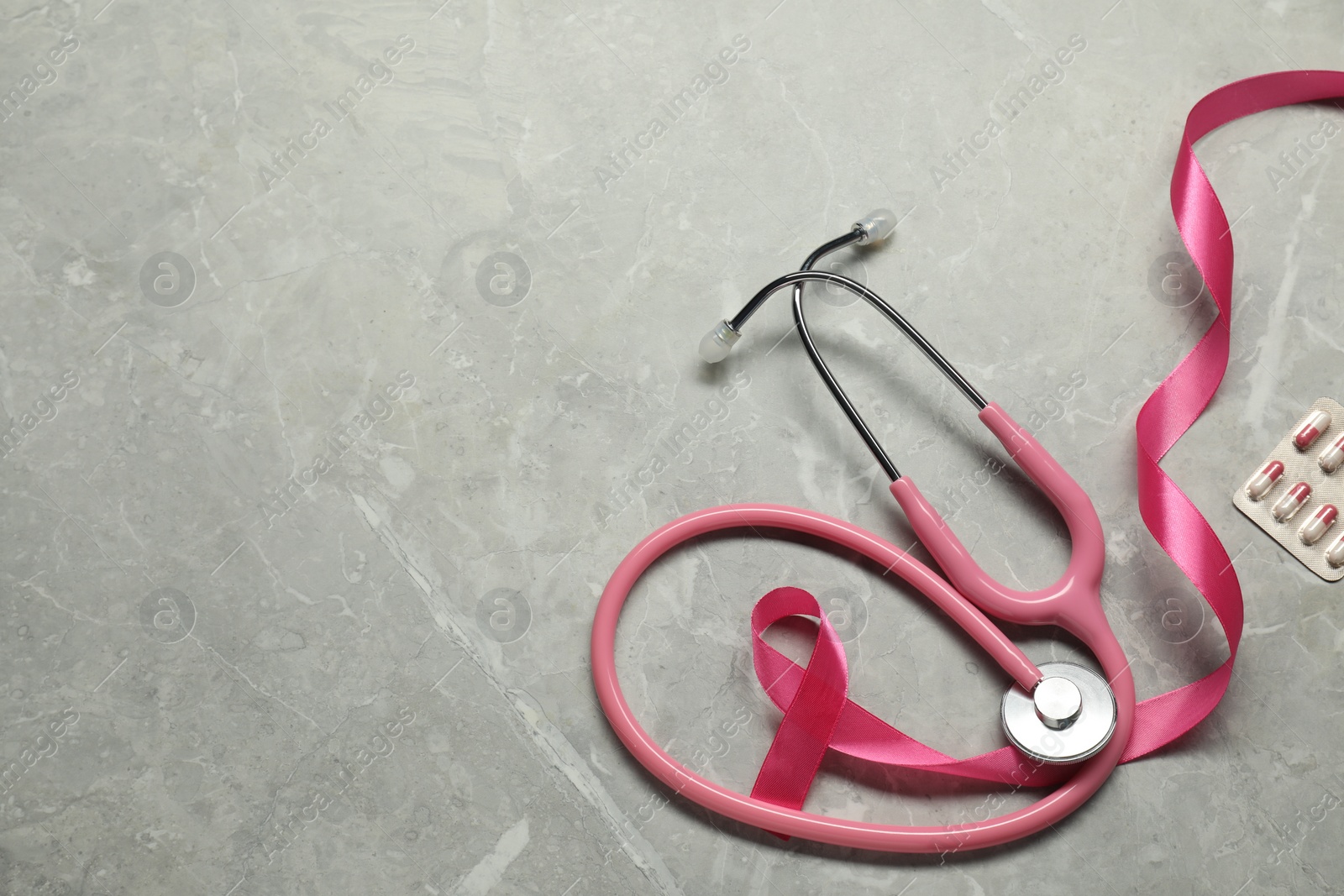 Photo of Breast cancer awareness. Pink ribbon, stethoscope and pills on grey marble table, flat lay. Space for text